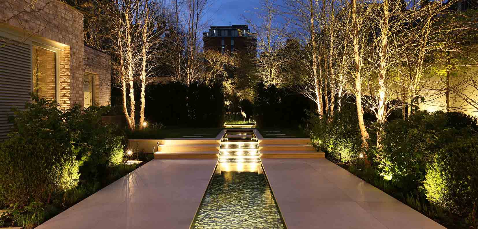 large garden with architectural gardens to uplight trees and water rill